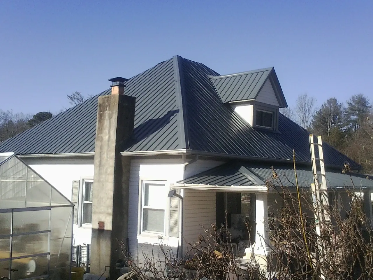 Dark blue standing seam metal roof on a white farmhouse with dormer in Mc Kinney