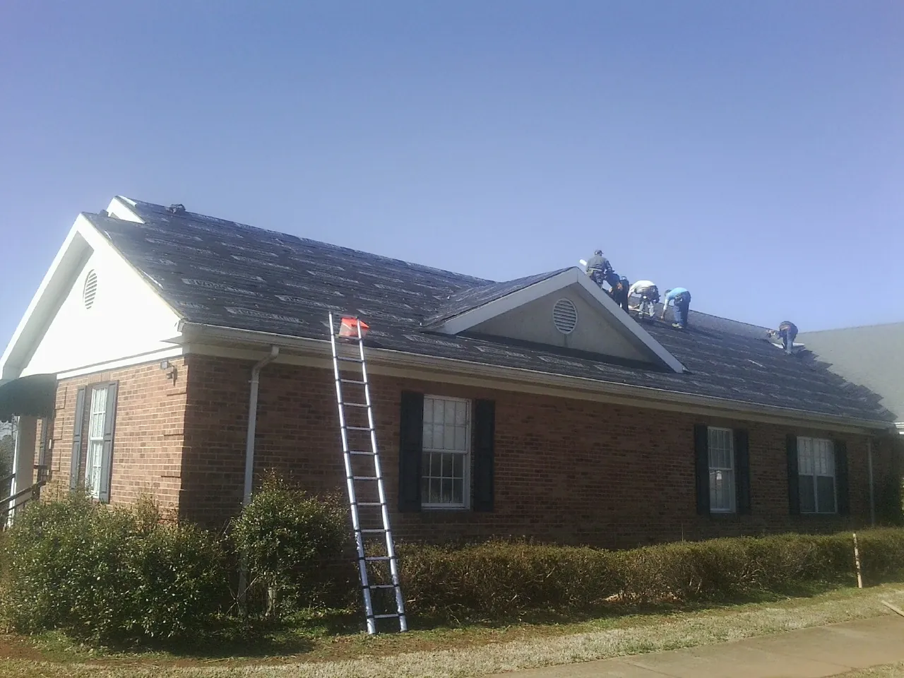 Crew tearing shingles off a brick ranch roof with a ladder set — Metal Roof Repair work by our crew in Mc Kinney