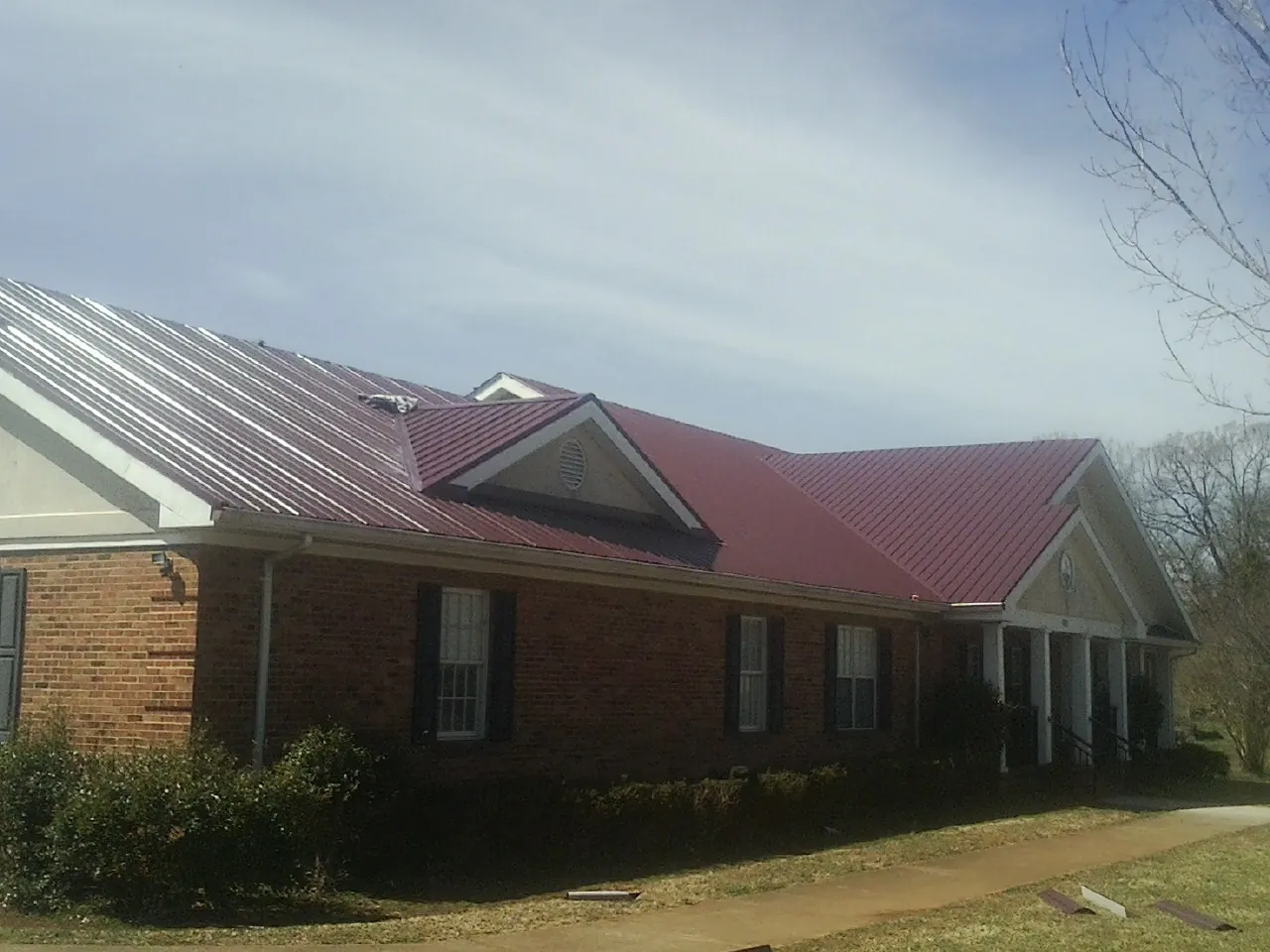 Red metal roof with gabled entries on a long brick building, from a Hail Damage Roof Repair job in Mc Kinney