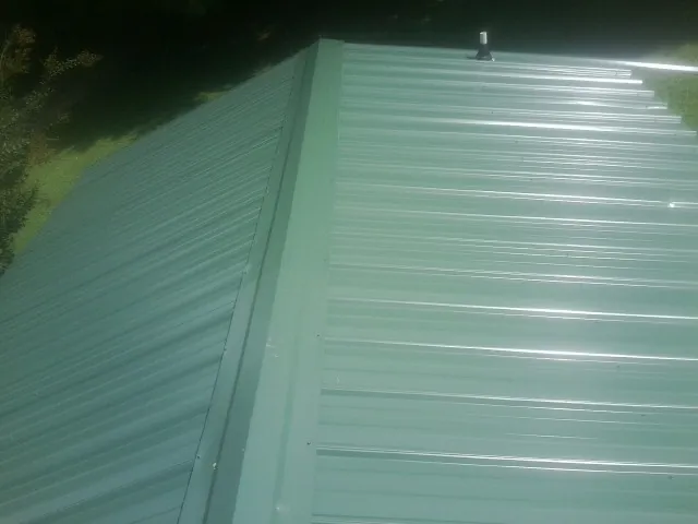 New green metal panels meeting at the ridge of a roof — Flat Roof Repair work by our crew in Mc Kinney