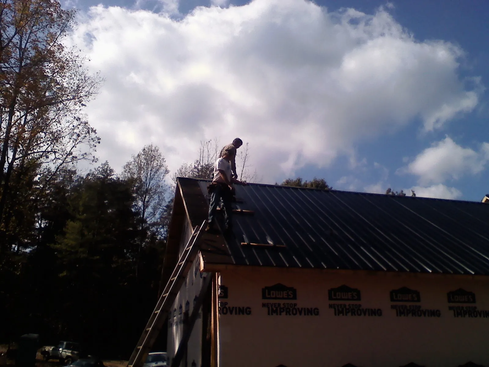 Roofer fastening dark metal panels high against a cloudy sky, from a Roof Inspection job in Mc Kinney