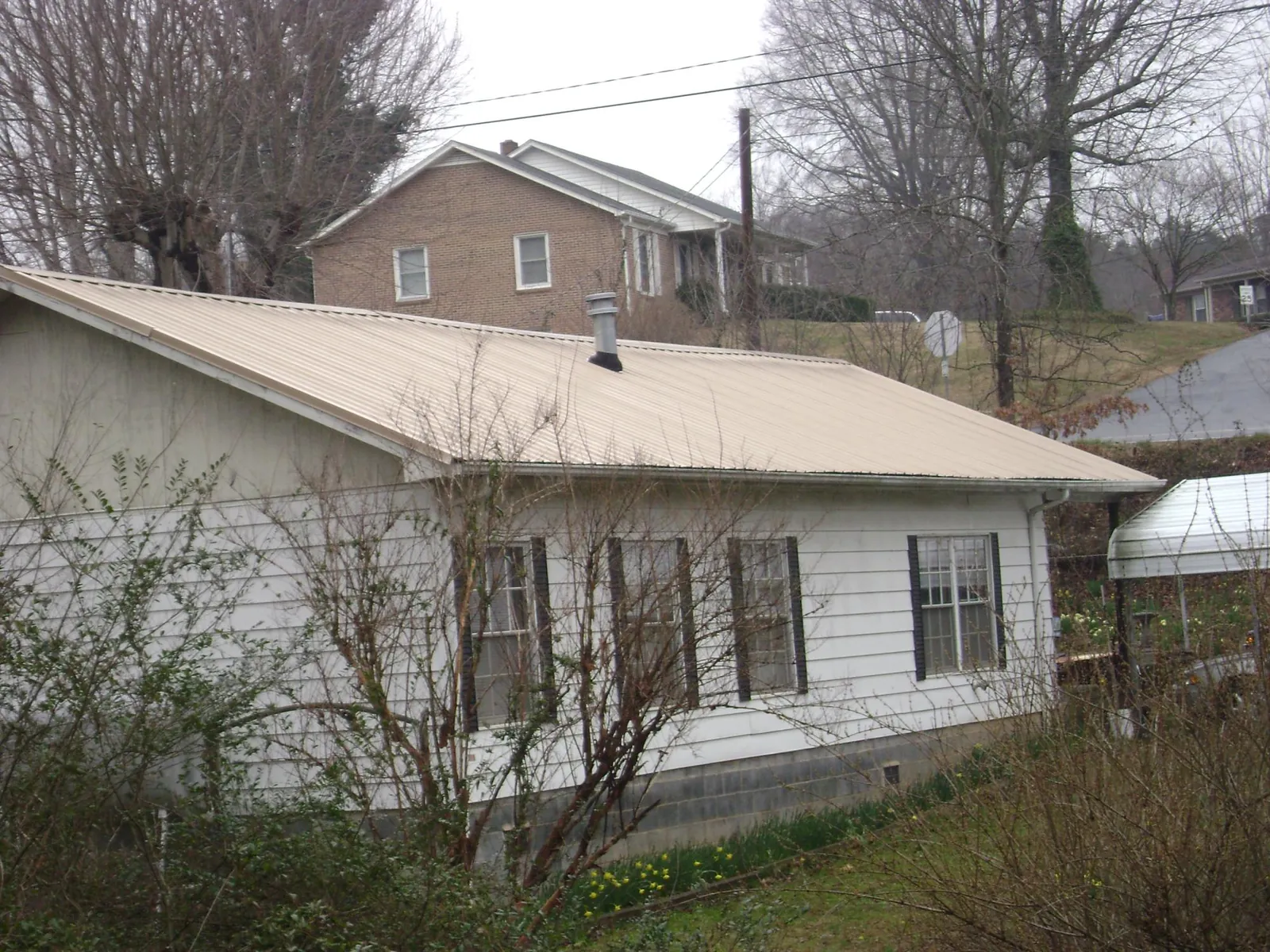 Tan metal roof on a white sided house set into a hillside — Commercial Roofing by Roofing Brothers in Mc Kinney