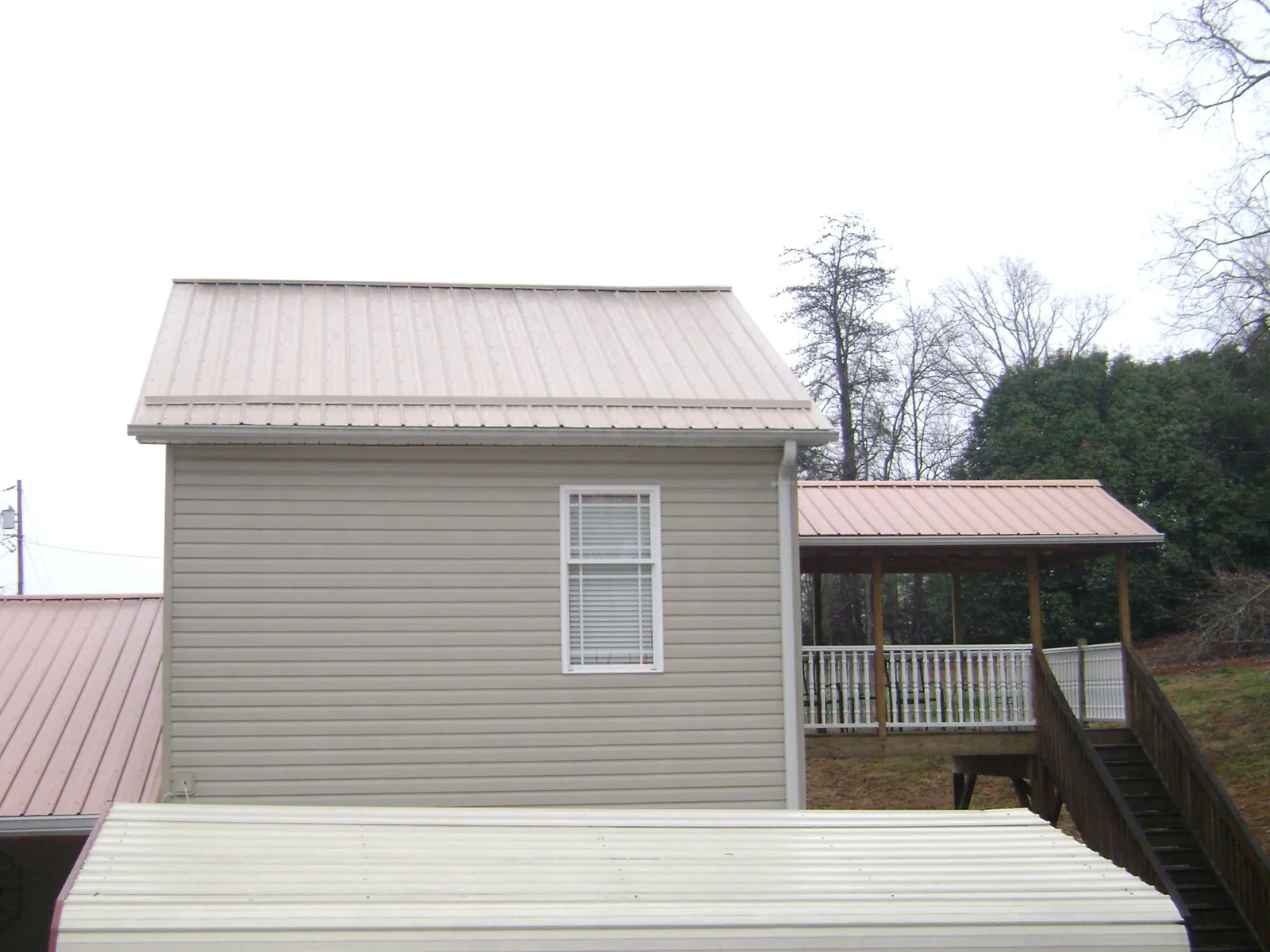 Tan metal roofs on a two story addition and attached porch, from a Roof Replacement job in Mc Kinney